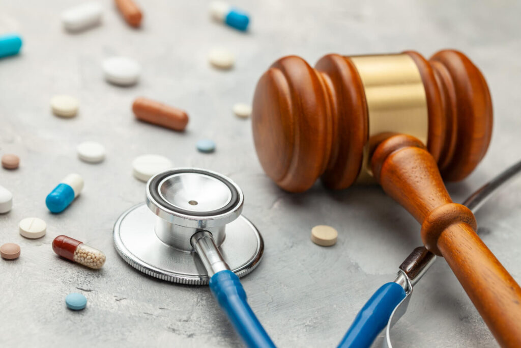 Stethoskop und Richterhammer zwischen verstreuten Medikamenten auf grauer Oberfläche